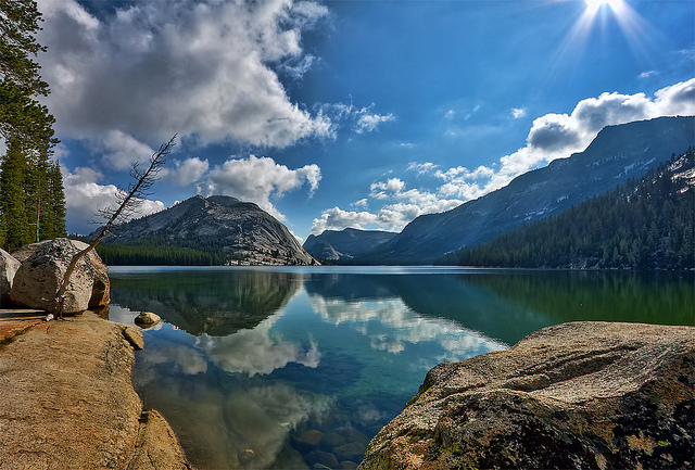A spectacular blue sky with some clouds is reflected upon Tenaya Lake, along with some mountains in the background.