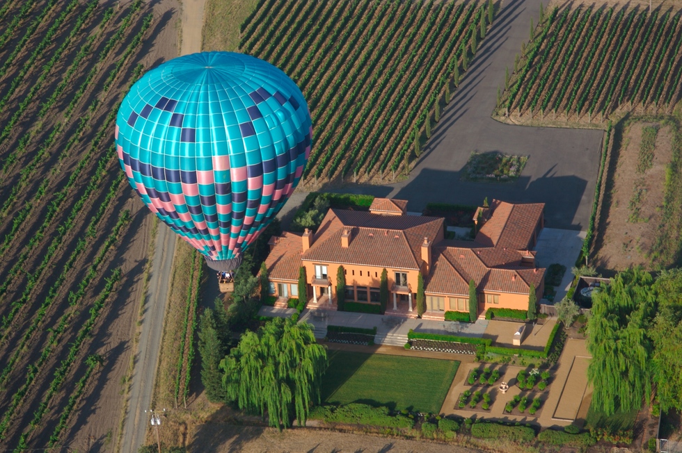 A hot air balloon flies over a winery in the Napa Valley