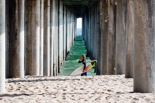 Surfer under a pier at Huntington Beach, California.
