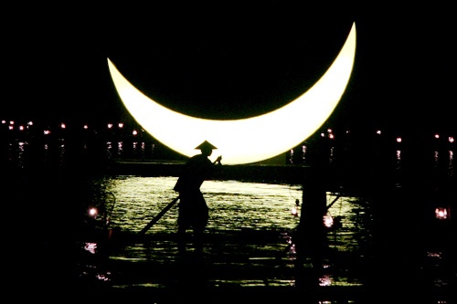 A cormorant fisherman rows his bamboo boat against the backdrop of a giant moon on the Li River,